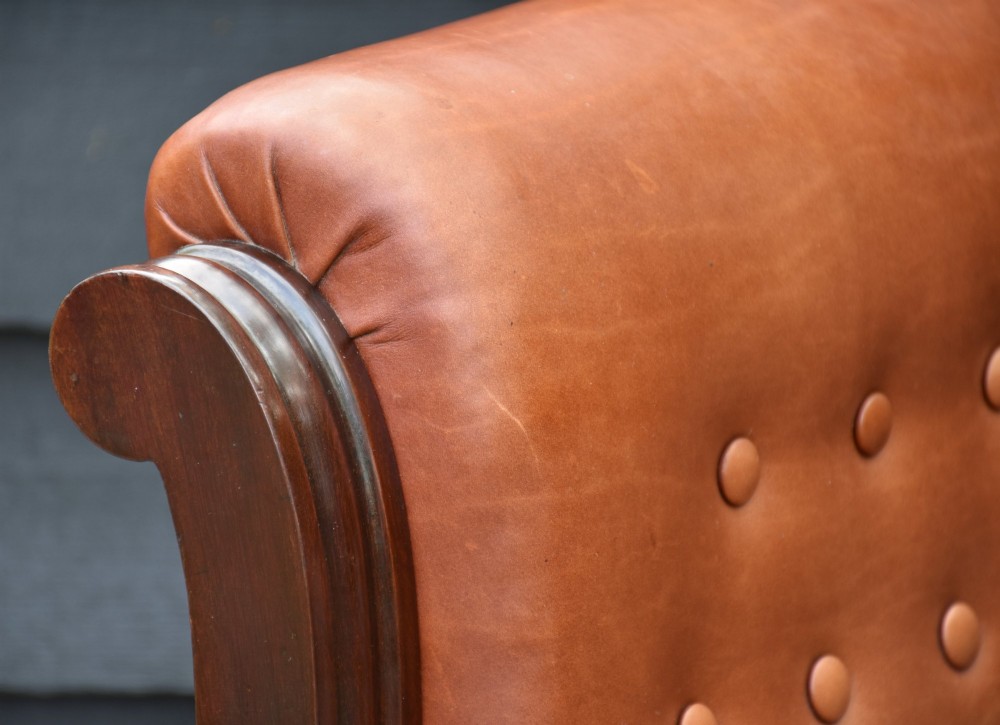 A 19th-century mahogany library armchair upholstered in buttoned brown leather with turned spindle arm supports and brass castors. View IV