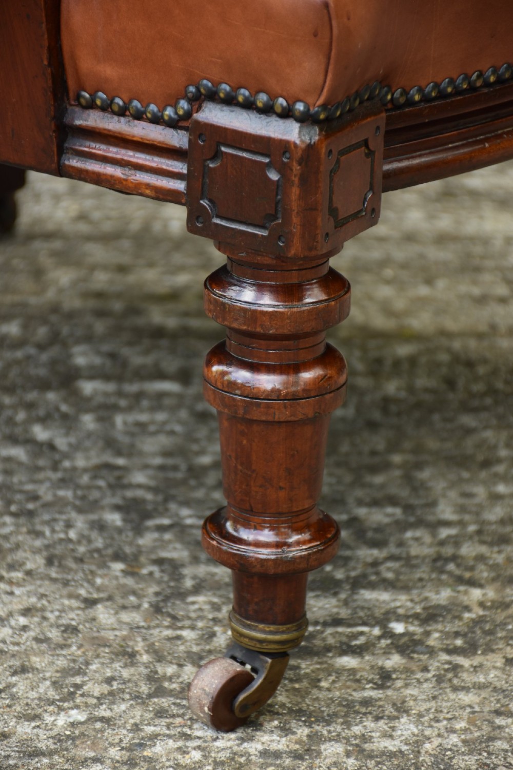 A 19th-century mahogany library armchair upholstered in buttoned brown leather with turned spindle arm supports and brass castors. View V