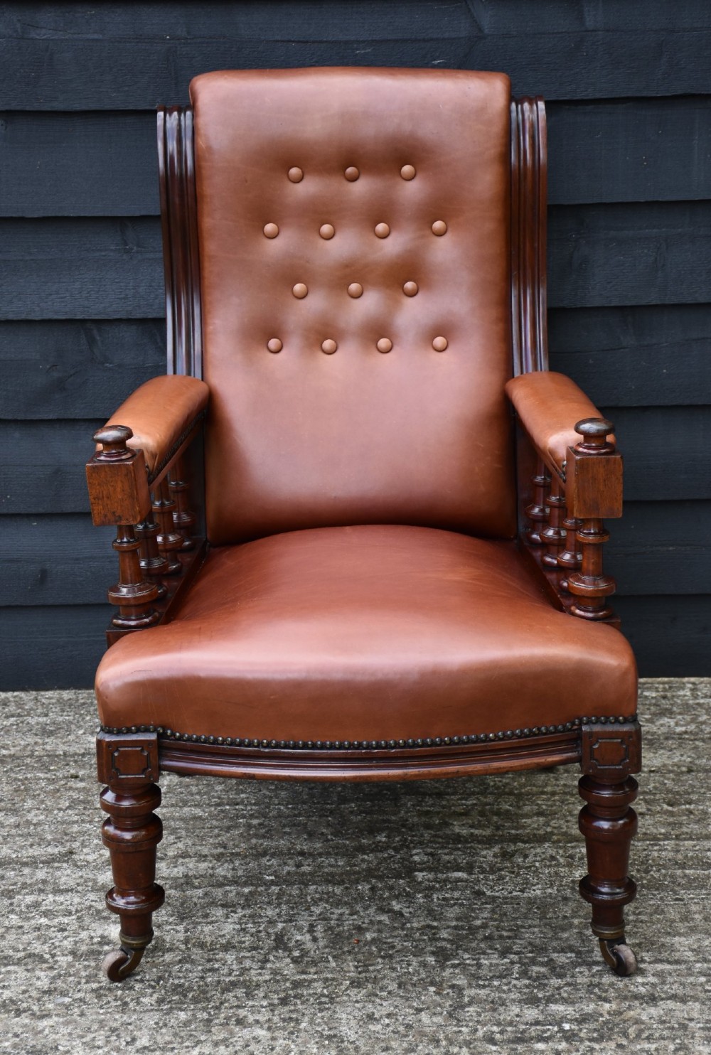 A 19th-century mahogany library armchair upholstered in buttoned brown leather with turned spindle arm supports and brass castors. View VI