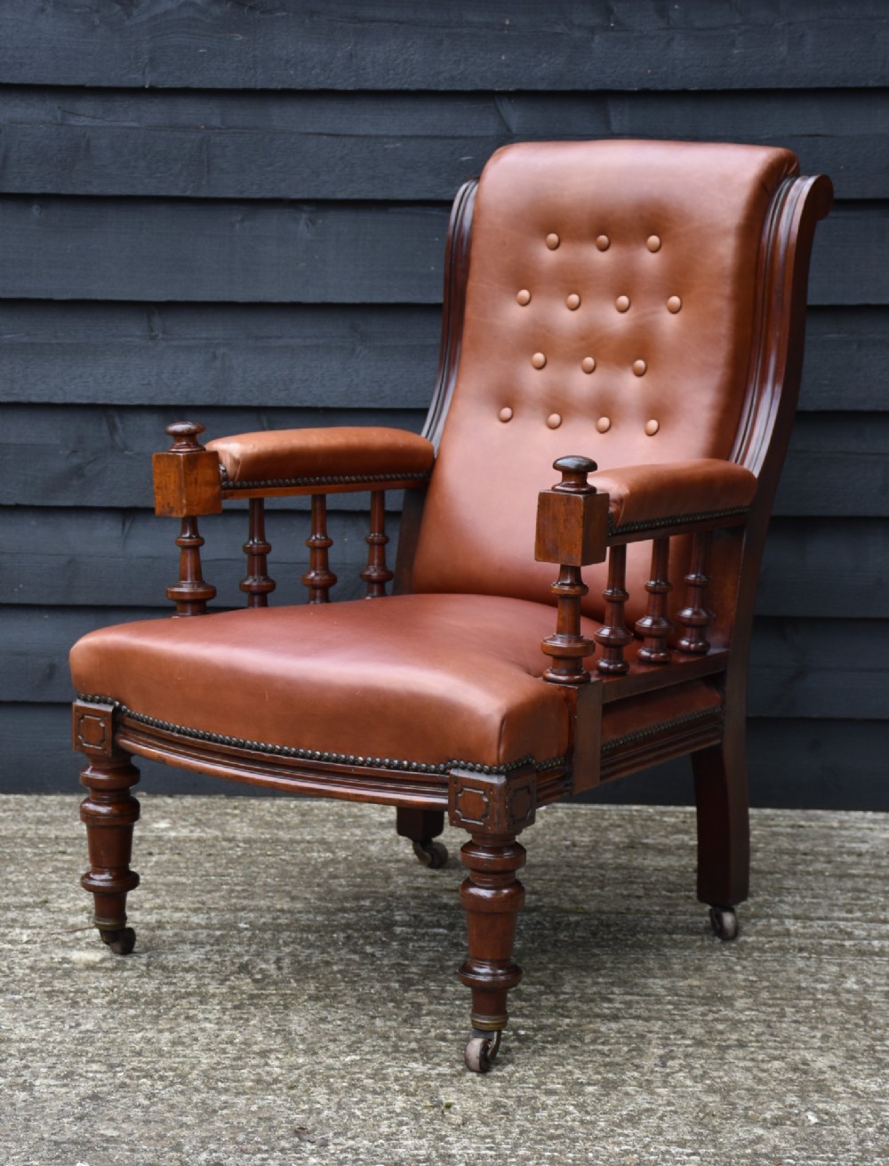 A 19th-century mahogany library armchair upholstered in buttoned brown leather with turned spindle arm supports and brass castors. View VII