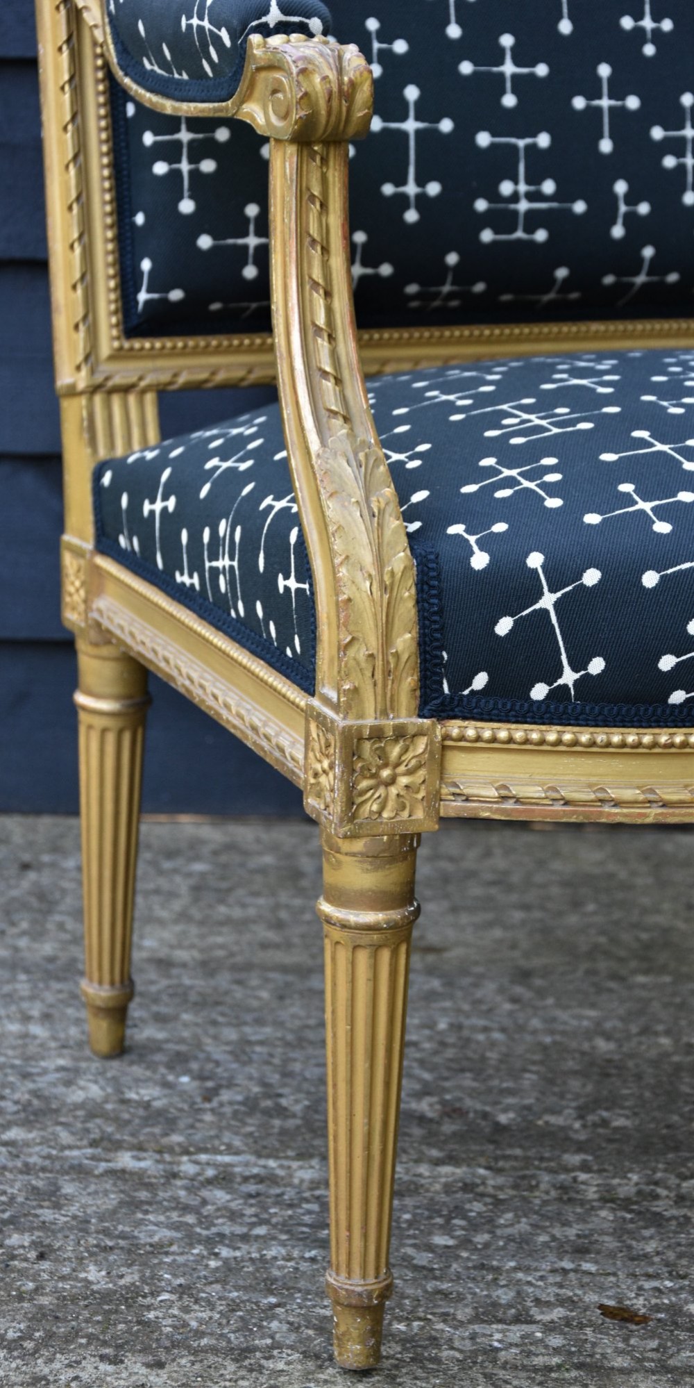 A French giltwood open armchair featuring a rectangular padded backrest, carved fluted legs, and navy blue upholstery with white geometric patterns. View II