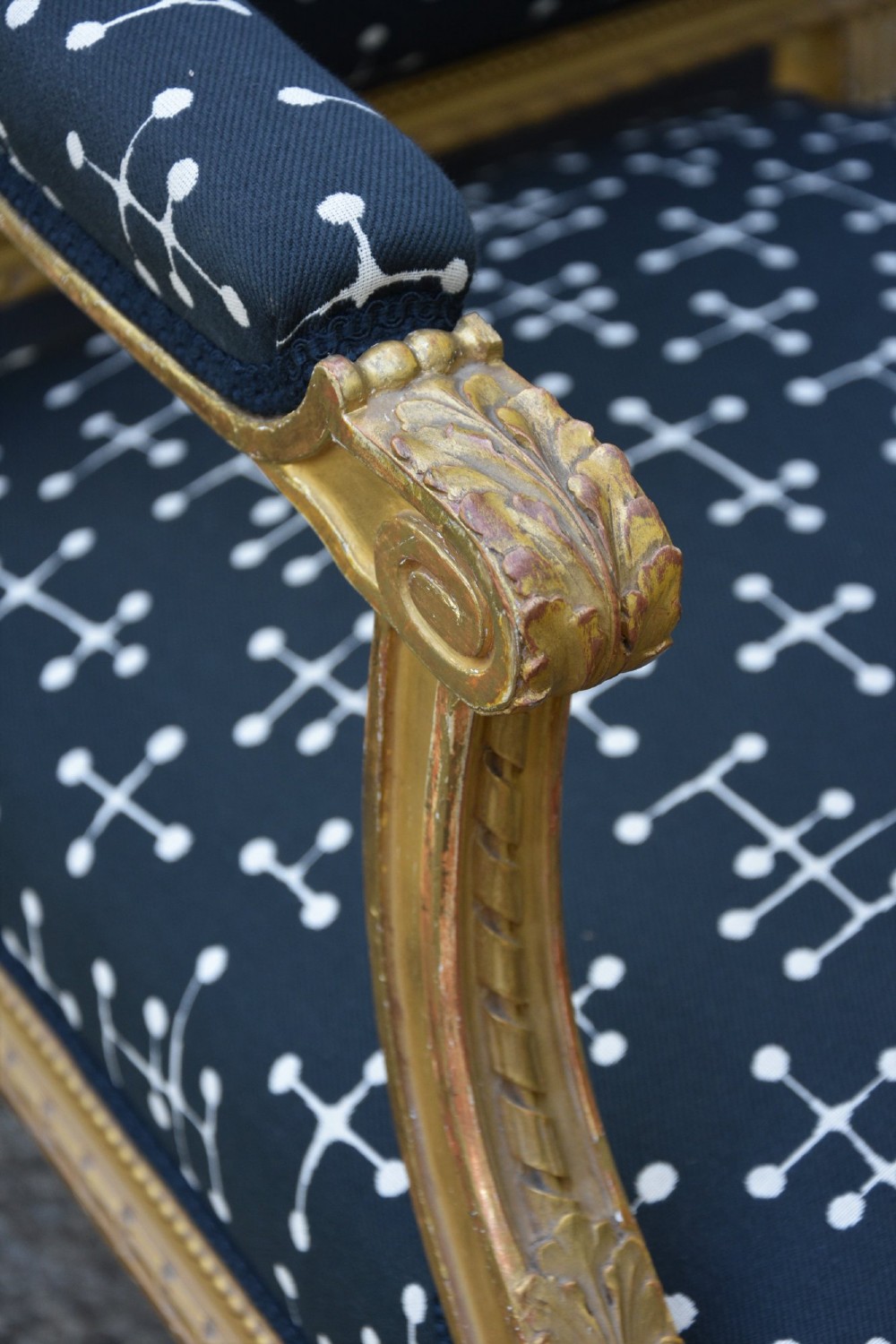 A French giltwood open armchair featuring a rectangular padded backrest, carved fluted legs, and navy blue upholstery with white geometric patterns. View III