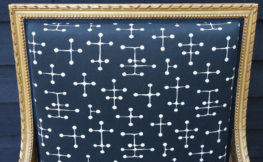A French giltwood open armchair featuring a rectangular padded backrest, carved fluted legs, and navy blue upholstery with white geometric patterns. View VI
