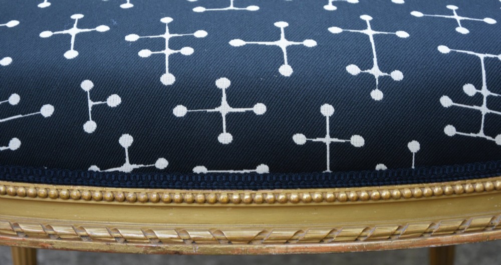 A French giltwood open armchair featuring a rectangular padded backrest, carved fluted legs, and navy blue upholstery with white geometric patterns. View VII