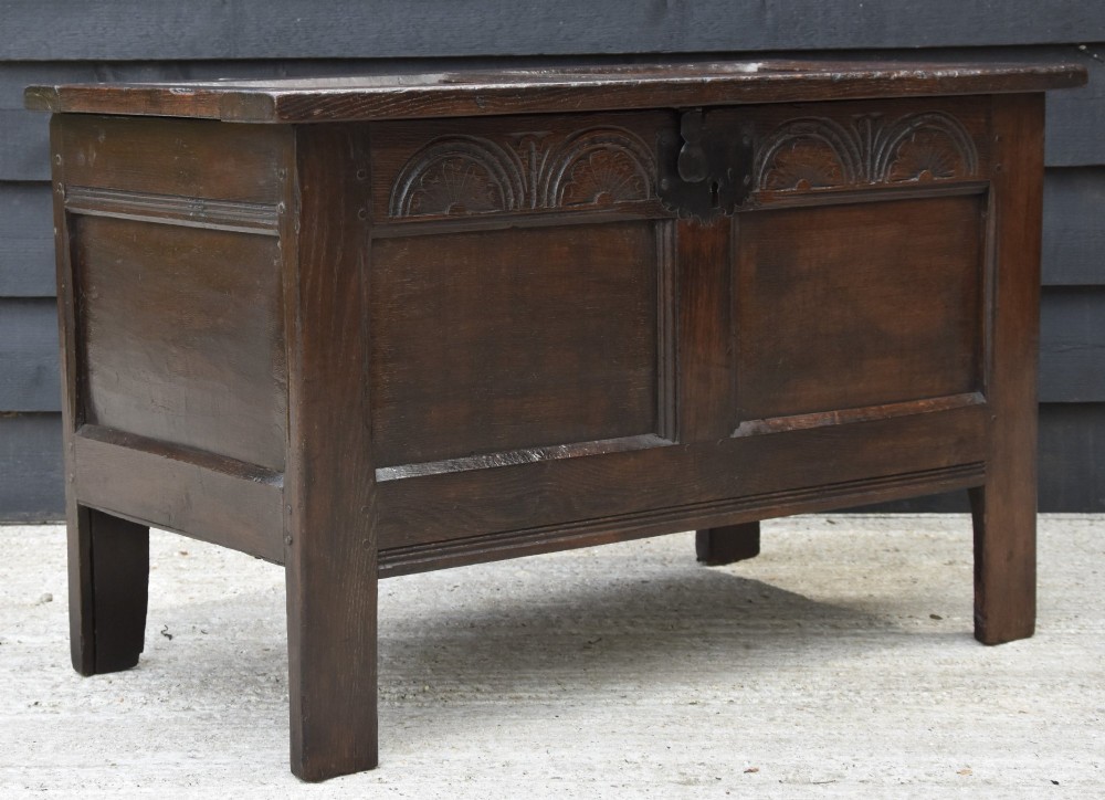 A small 17th-century dark oak coffer with a carved lunette frieze, twin front panels, peg joints, and a wrought iron lock plate.