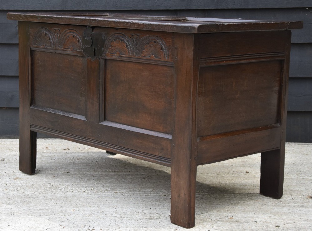 A small 17th-century dark oak coffer with a carved lunette frieze, twin front panels, peg joints, and a wrought iron lock plate. View V
