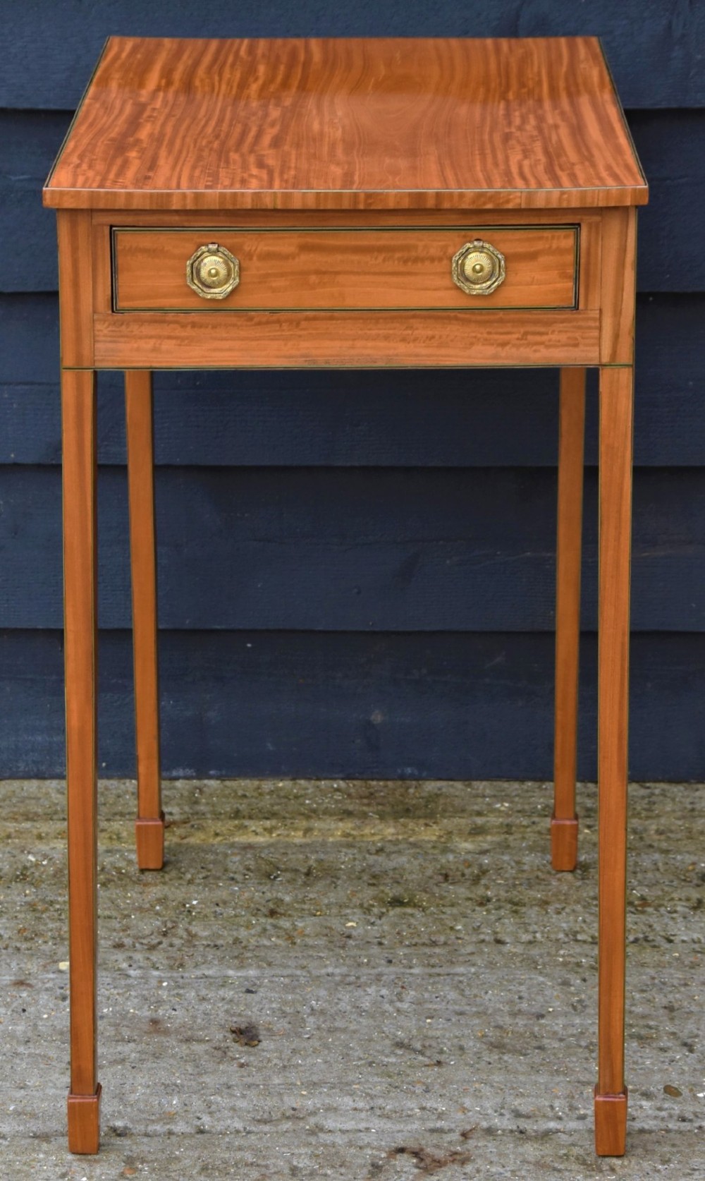 An antique Georgian satinwood lamp table featuring a single drawer with octagonal brass ring handles and slim square tapered legs.