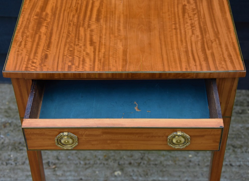 An antique Georgian satinwood lamp table featuring a single drawer with octagonal brass ring handles and slim square tapered legs. View VII