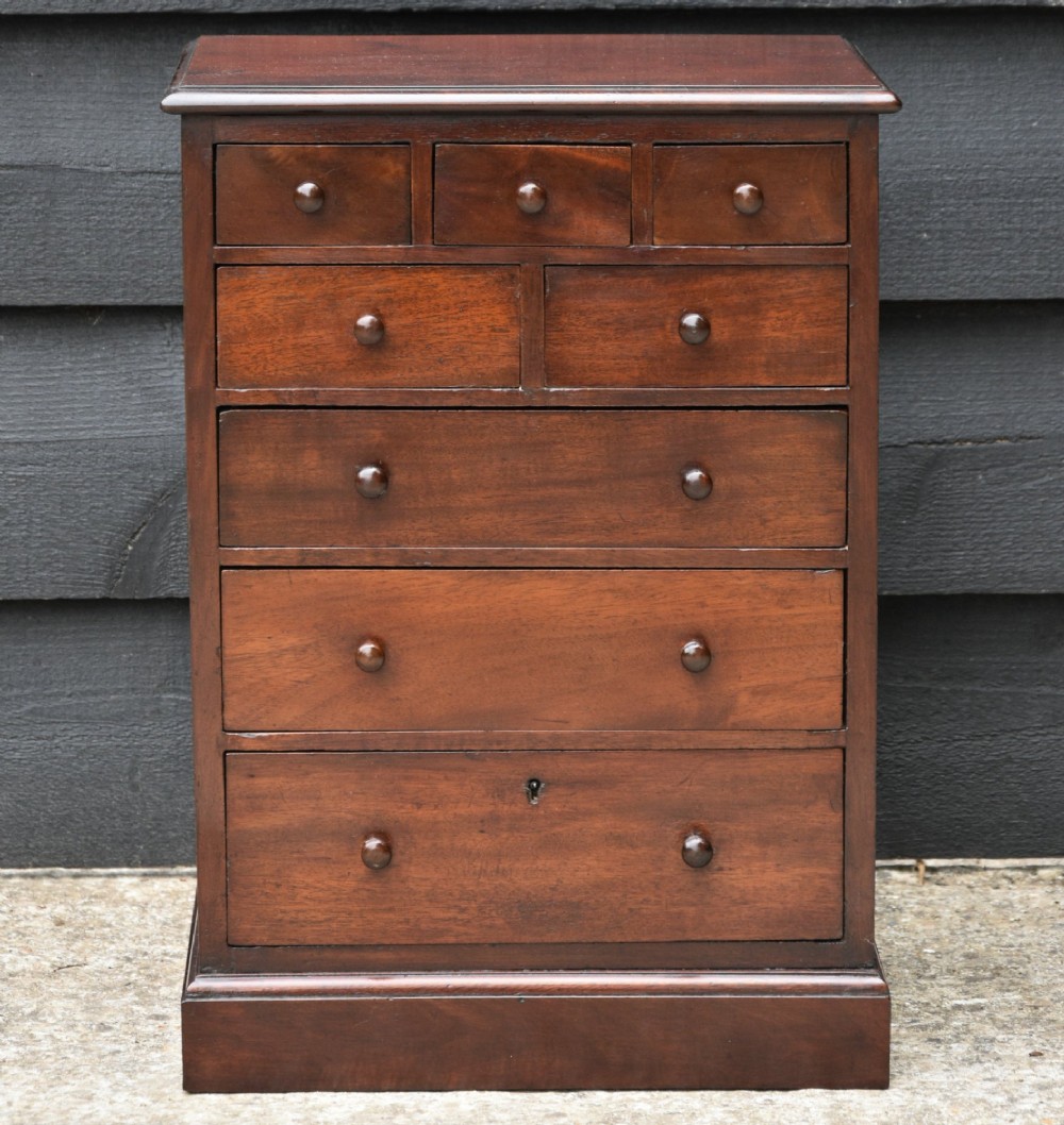 A Victorian mahogany miniature chest of drawers featuring eight drawers with turned wooden knobs and a solid plinth base.