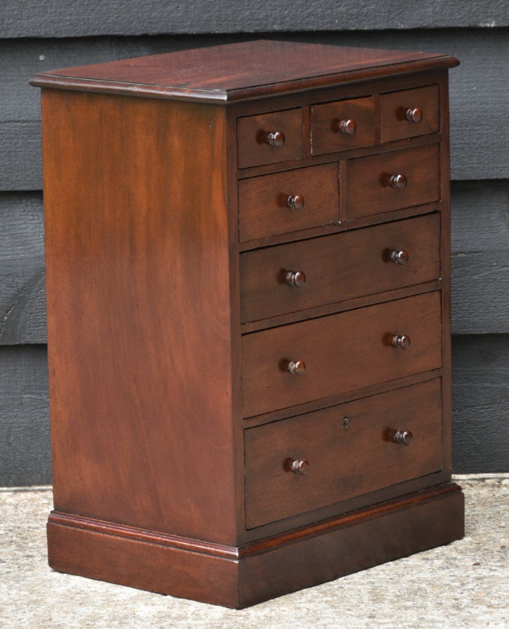 A Victorian mahogany miniature chest of drawers featuring eight drawers with turned wooden knobs and a solid plinth base. View II