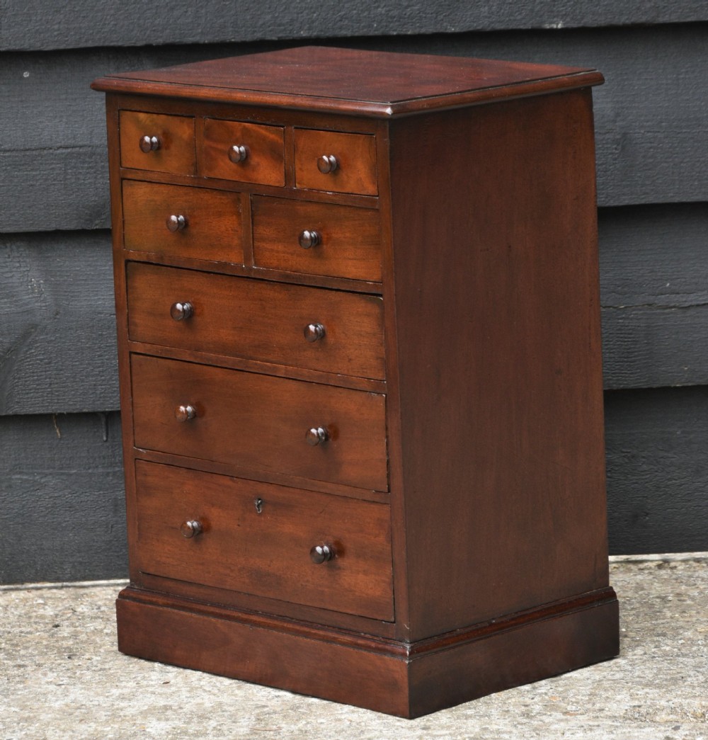 A Victorian mahogany miniature chest of drawers featuring eight drawers with turned wooden knobs and a solid plinth base. View III