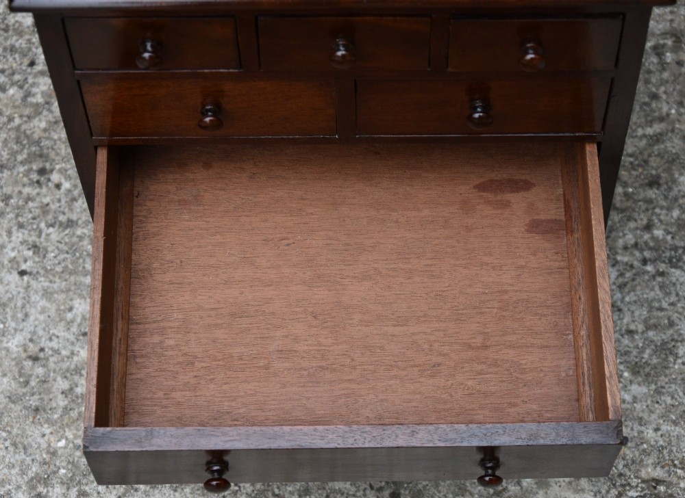 A Victorian mahogany miniature chest of drawers featuring eight drawers with turned wooden knobs and a solid plinth base. View VI
