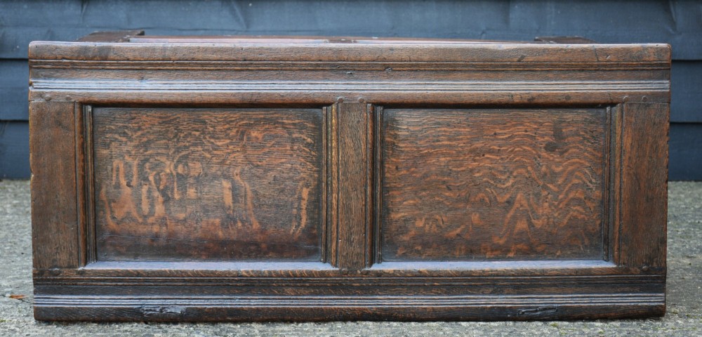 A seventeenth-century oak coffer featuring a twin-panelled front, moulded lid, stile legs, and a central iron keyhole escutcheon. View V