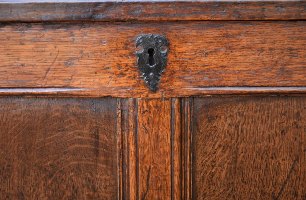 A seventeenth-century oak coffer featuring a twin-panelled front, moulded lid, stile legs, and a central iron keyhole escutcheon. View VII
