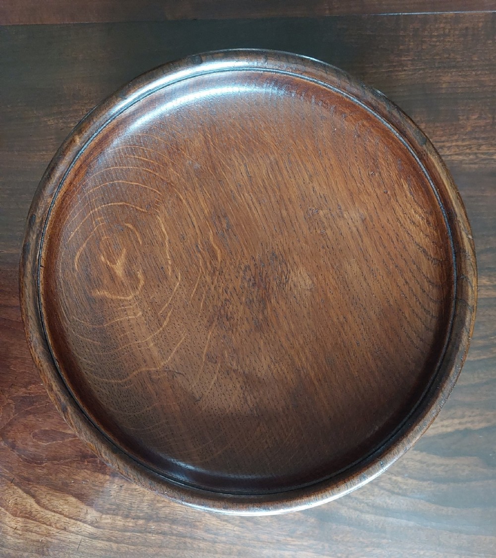 A circular dark carved oak fruit bowl on a low pedestal base decorated with a relief band of carved grapevines. View III