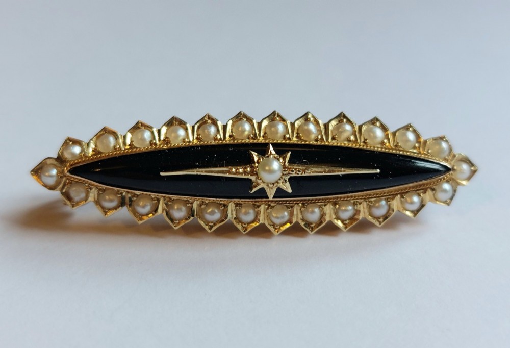 An elongated navette-shaped Victorian 15ct gold brooch with a black onyx center, central seed pearl starburst, and seed pearl border.