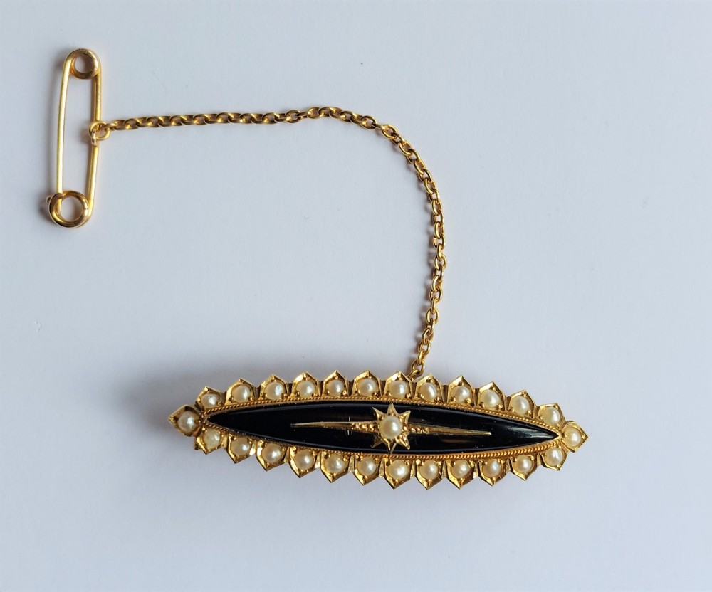 An elongated navette-shaped Victorian 15ct gold brooch with a black onyx center, central seed pearl starburst, and seed pearl border. View II