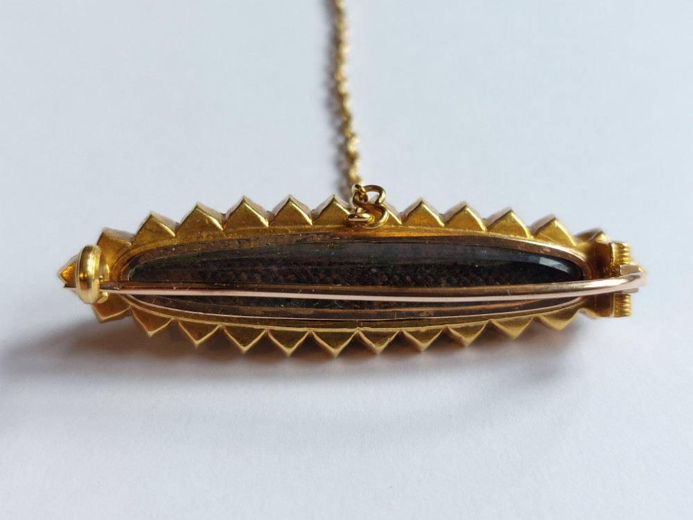 An elongated navette-shaped Victorian 15ct gold brooch with a black onyx center, central seed pearl starburst, and seed pearl border. View III