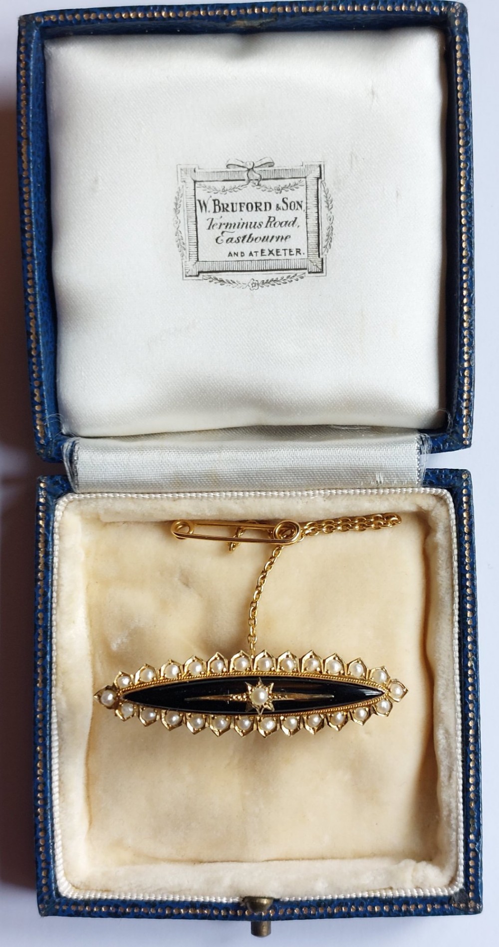 An elongated navette-shaped Victorian 15ct gold brooch with a black onyx center, central seed pearl starburst, and seed pearl border. View V