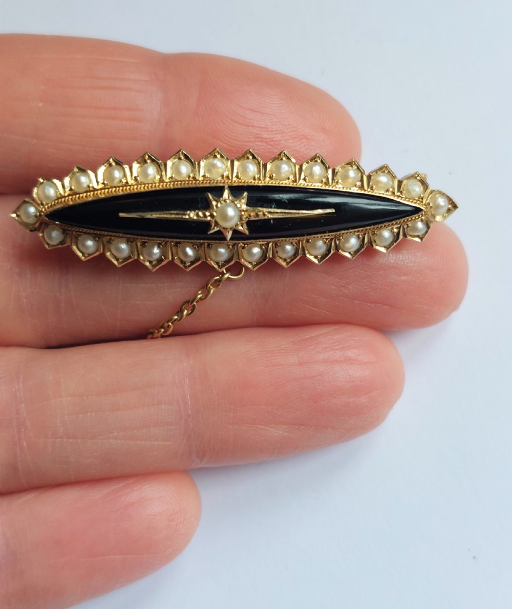 An elongated navette-shaped Victorian 15ct gold brooch with a black onyx center, central seed pearl starburst, and seed pearl border. View VII