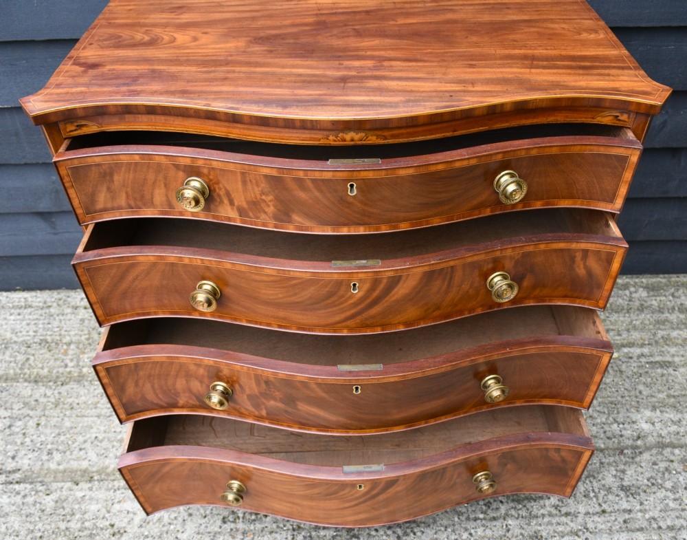 A late 18th-century Georgian mahogany serpentine chest of drawers featuring four graduated drawers with brass handles and bracket feet. View V