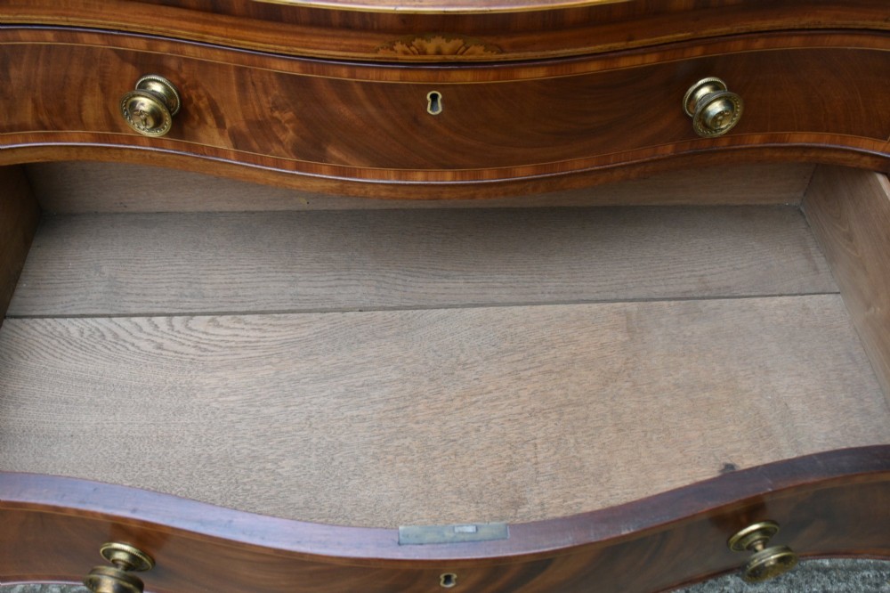 A late 18th-century Georgian mahogany serpentine chest of drawers featuring four graduated drawers with brass handles and bracket feet. View VIII