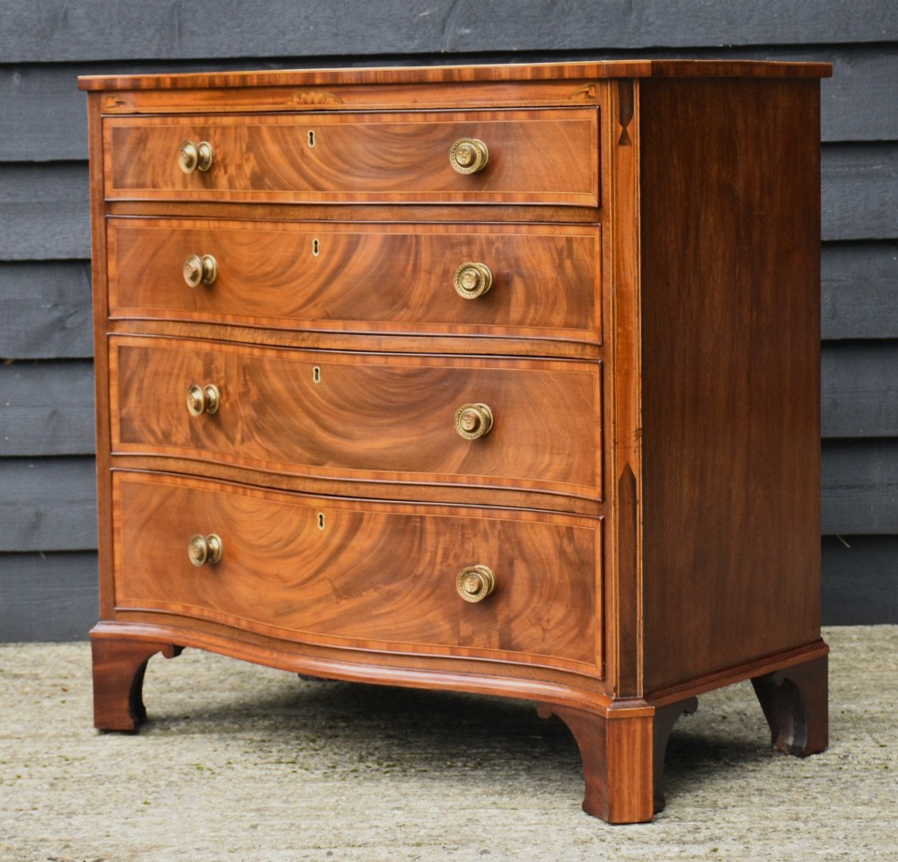 A late 18th-century Georgian mahogany serpentine chest of drawers featuring four graduated drawers with brass handles and bracket feet. View X