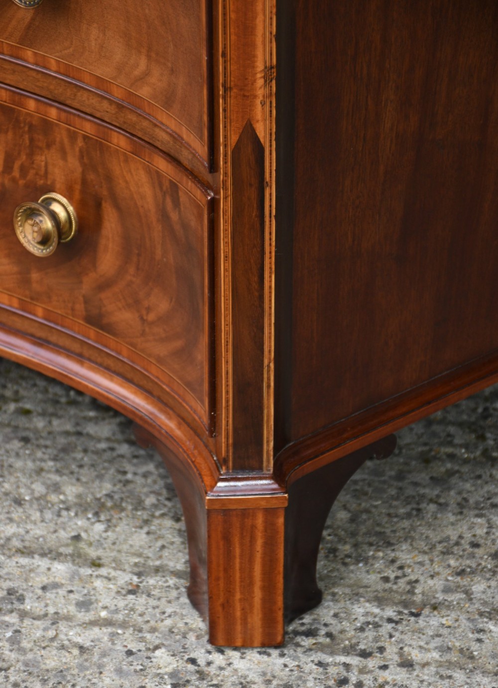 A late 18th-century Georgian mahogany serpentine chest of drawers featuring four graduated drawers with brass handles and bracket feet. View XI