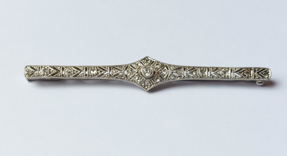 An Art Deco elongated platinum bar brooch adorned with milgrain-bordered geometric openwork and central diamonds.