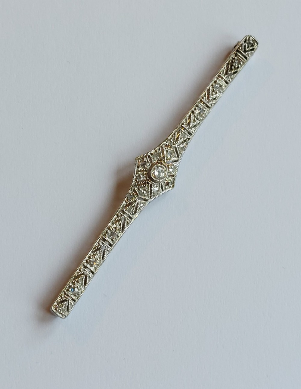An Art Deco elongated platinum bar brooch adorned with milgrain-bordered geometric openwork and central diamonds. View II