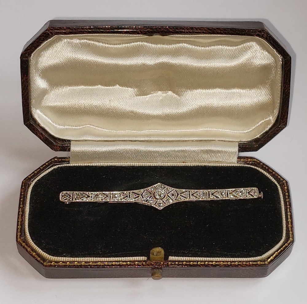 An Art Deco elongated platinum bar brooch adorned with milgrain-bordered geometric openwork and central diamonds. View VI