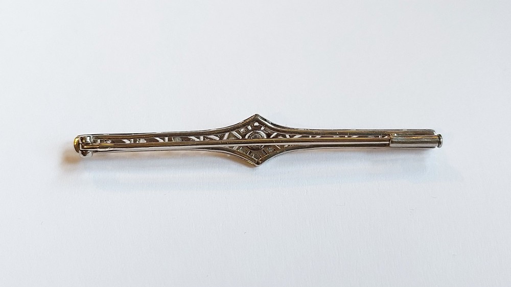 An Art Deco elongated platinum bar brooch adorned with milgrain-bordered geometric openwork and central diamonds. View VII