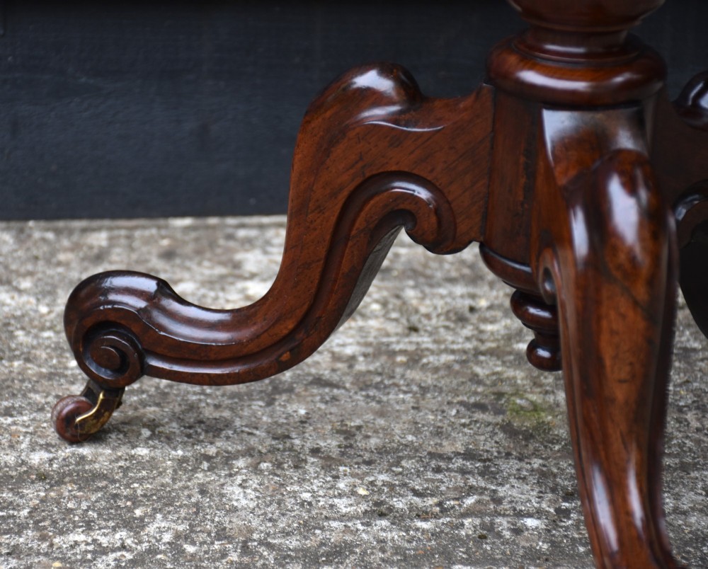 A circular 19th-century rosewood lamp table featuring a bookmatched wood grain top resting on a carved pedestal stem with tripod legs. View III