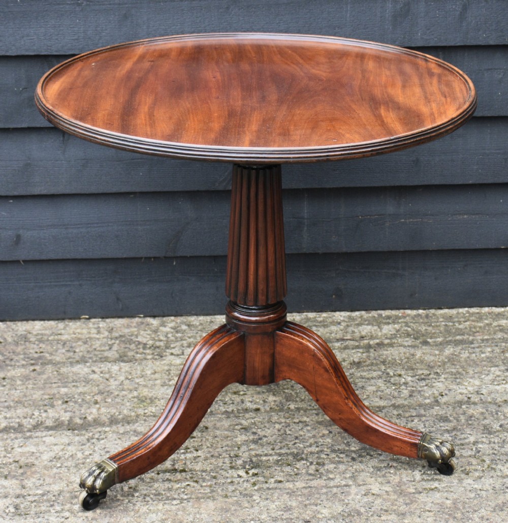 A circular Regency mahogany tea table featuring a moulded edge top, fluted central pedestal, and three reeded tripod legs with brass paw feet and castors.