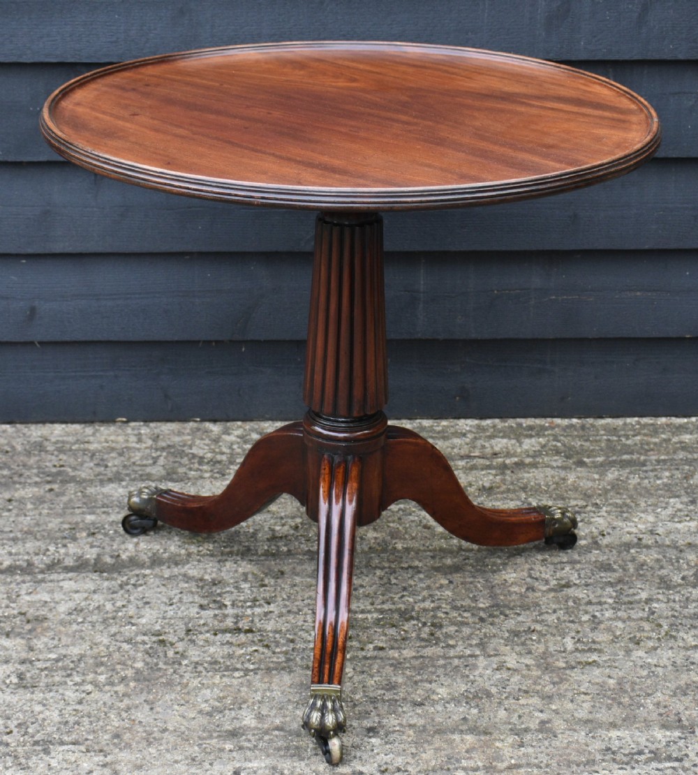 A circular Regency mahogany tea table featuring a moulded edge top, fluted central pedestal, and three reeded tripod legs with brass paw feet and castors. View II