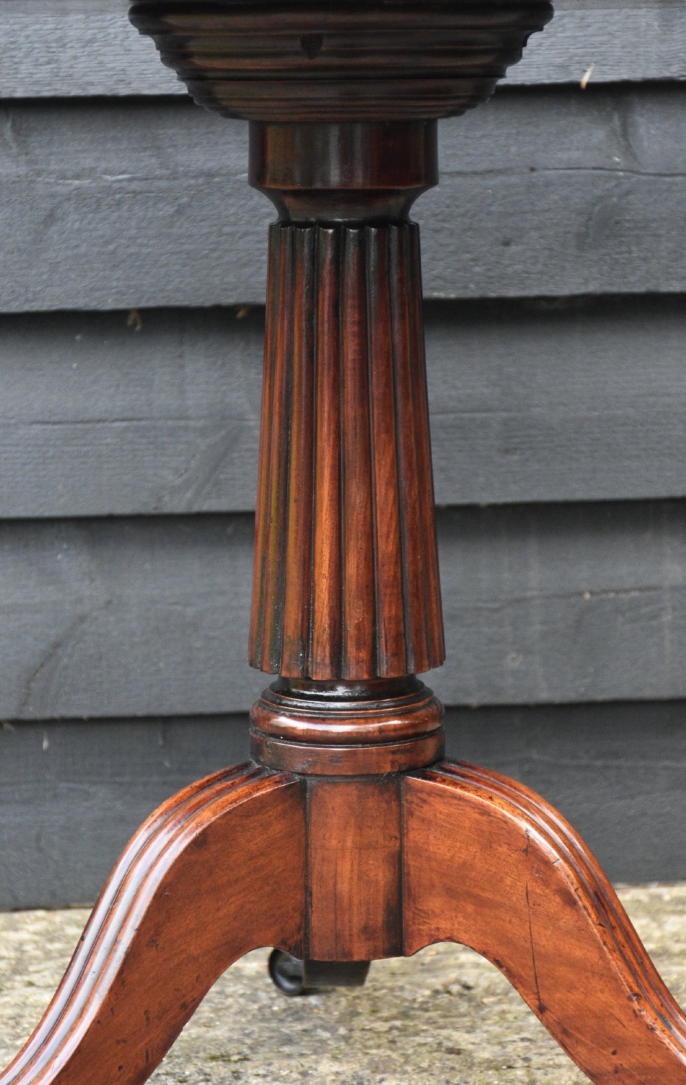 A circular Regency mahogany tea table featuring a moulded edge top, fluted central pedestal, and three reeded tripod legs with brass paw feet and castors. View III