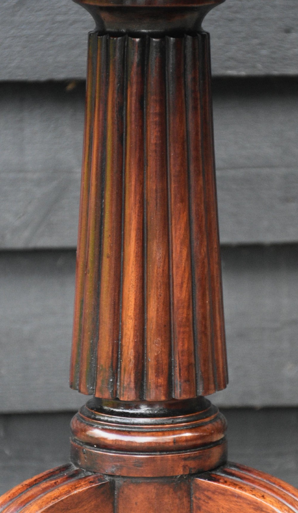 A circular Regency mahogany tea table featuring a moulded edge top, fluted central pedestal, and three reeded tripod legs with brass paw feet and castors. View IV