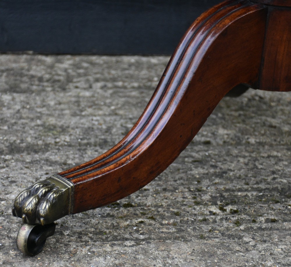 A circular Regency mahogany tea table featuring a moulded edge top, fluted central pedestal, and three reeded tripod legs with brass paw feet and castors. View V