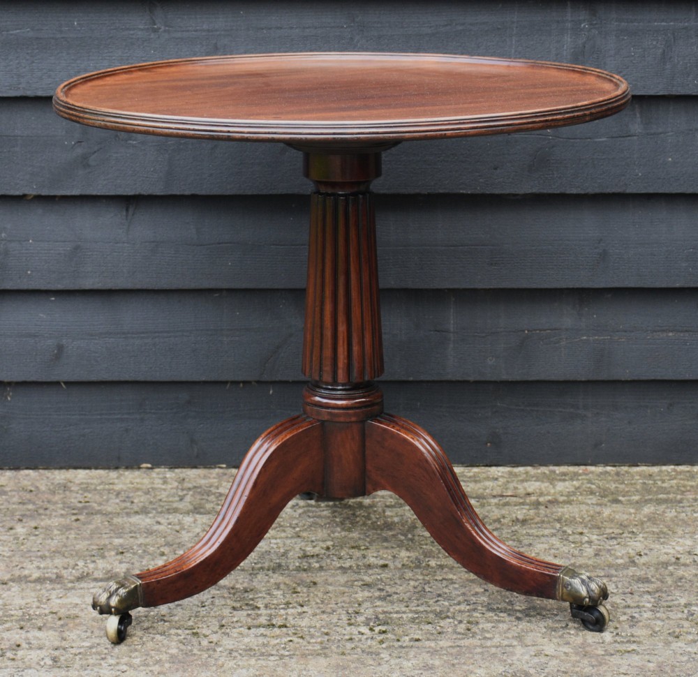 A circular Regency mahogany tea table featuring a moulded edge top, fluted central pedestal, and three reeded tripod legs with brass paw feet and castors. View VIII