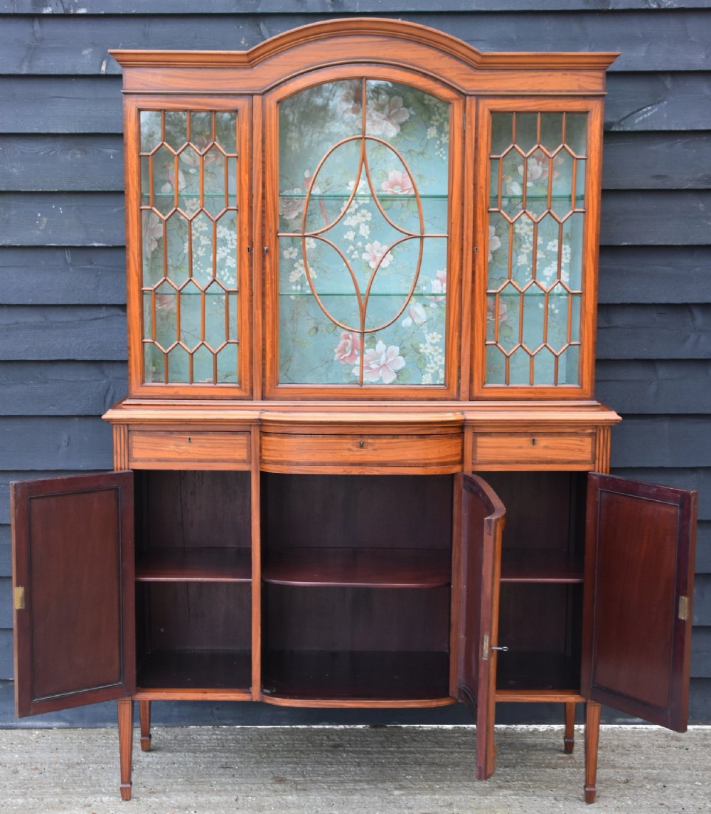 An Edwardian satinwood display cabinet featuring three astragal glazed doors, floral fabric interior lining, and inlaid lower cupboard doors raised on square tapered legs. View II