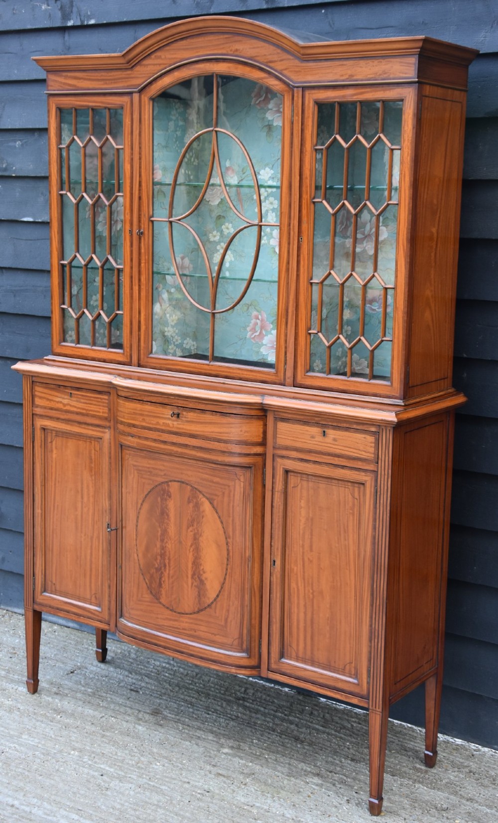 An Edwardian satinwood display cabinet featuring three astragal glazed doors, floral fabric interior lining, and inlaid lower cupboard doors raised on square tapered legs. View III