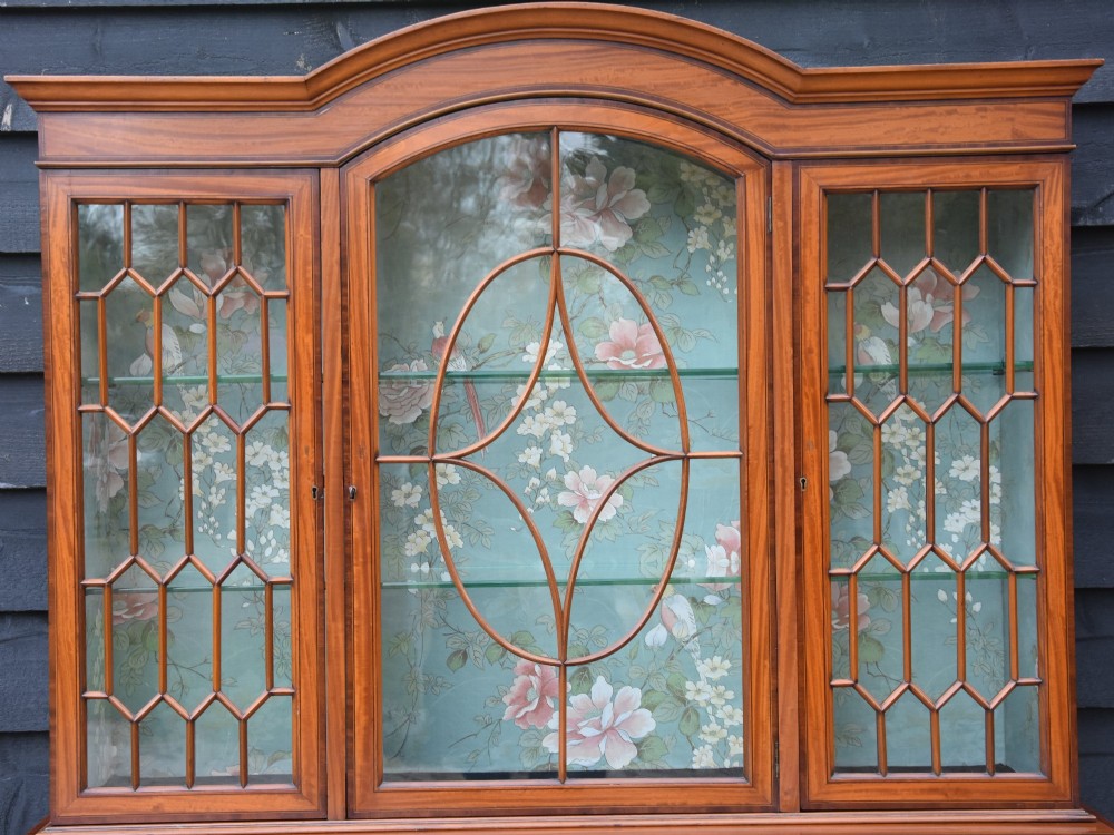 An Edwardian satinwood display cabinet featuring three astragal glazed doors, floral fabric interior lining, and inlaid lower cupboard doors raised on square tapered legs. View V
