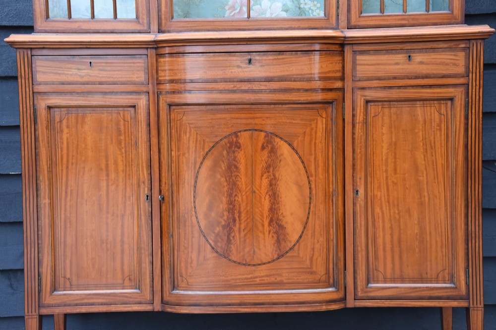 An Edwardian satinwood display cabinet featuring three astragal glazed doors, floral fabric interior lining, and inlaid lower cupboard doors raised on square tapered legs. View VIII