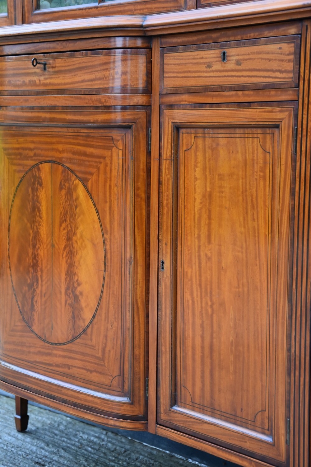 An Edwardian satinwood display cabinet featuring three astragal glazed doors, floral fabric interior lining, and inlaid lower cupboard doors raised on square tapered legs. View IX