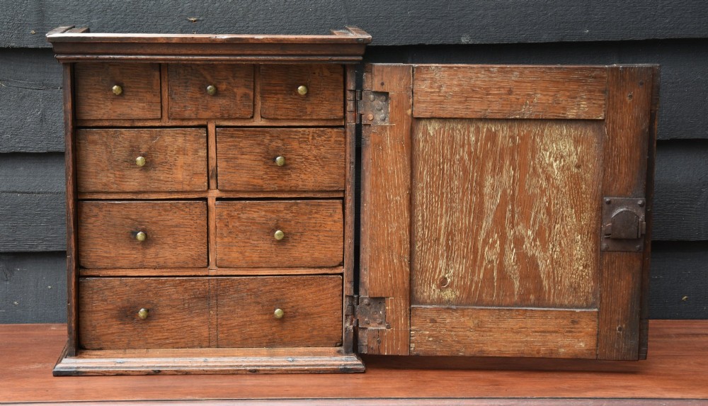 An early 18th-century oak spice cupboard featuring a single fielded panel door, brass escutcheon, and moulded top and base trim. View II