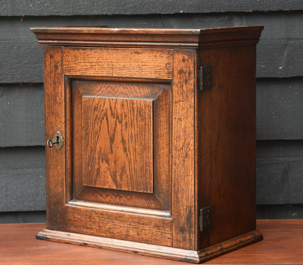 An early 18th-century oak spice cupboard featuring a single fielded panel door, brass escutcheon, and moulded top and base trim. View VIII