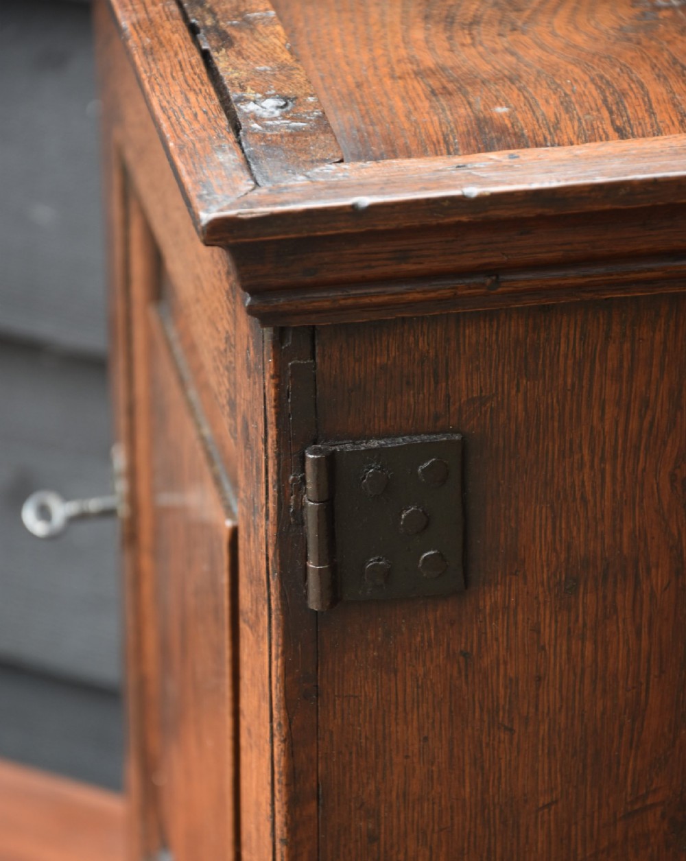 An early 18th-century oak spice cupboard featuring a single fielded panel door, brass escutcheon, and moulded top and base trim. View X