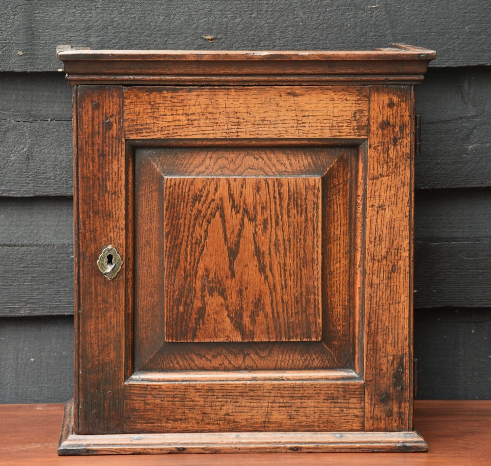 An early 18th-century oak spice cupboard featuring a single fielded panel door, brass escutcheon, and moulded top and base trim. View XI