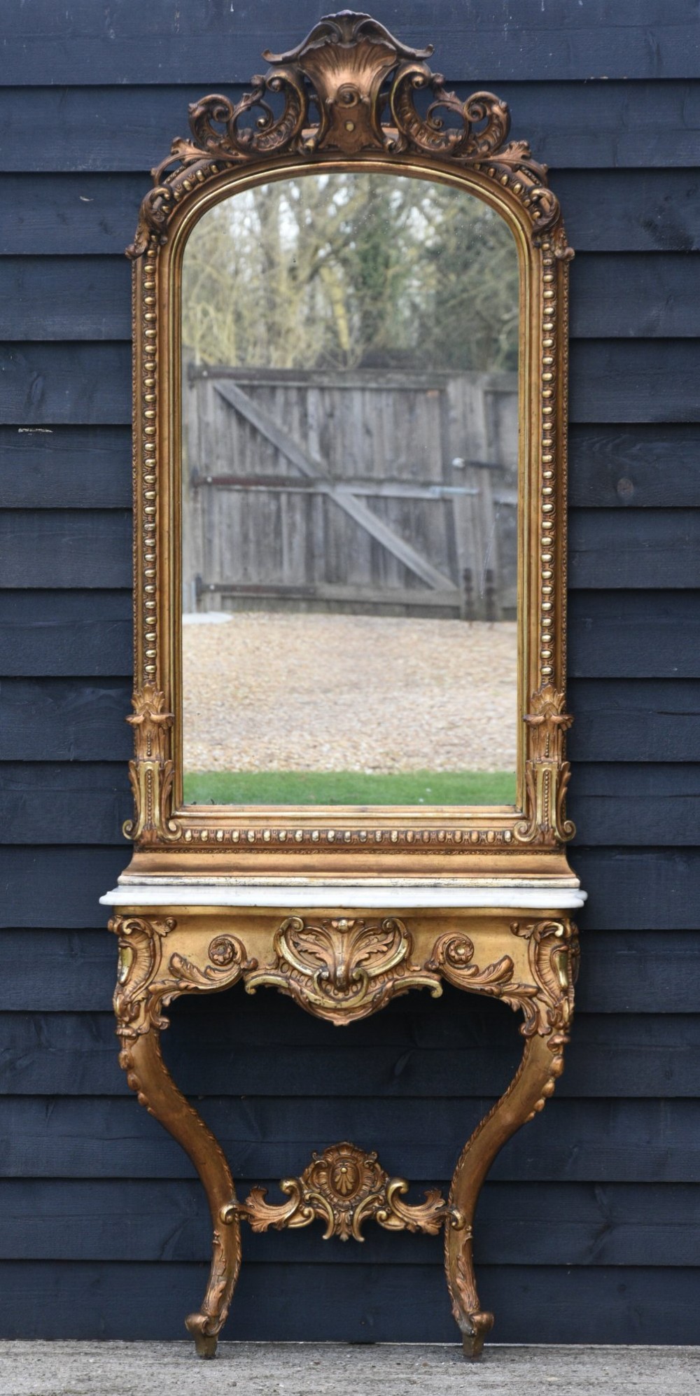 A French giltwood pier mirror featuring a carved rocaille cresting, mounted above a matching marble-topped console table with cabriole legs.