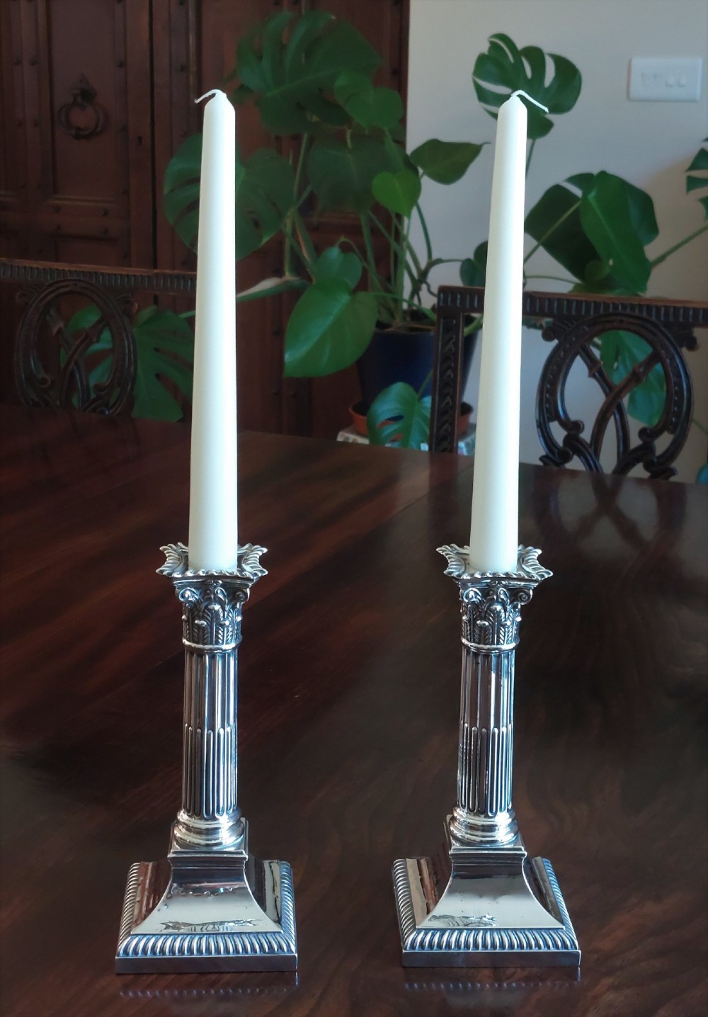 A pair of sterling silver candlesticks designed in the form of Corinthian columns with fluted shafts and stepped square bases holding white taper candles.